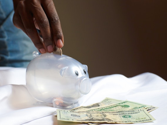 hand placing coins into a clear big bank